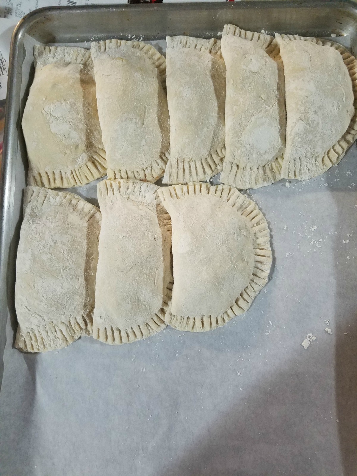 Uncooked hand pies layered on a half sheet pan.