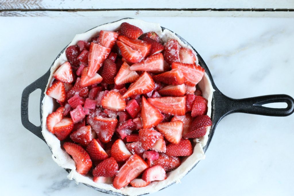 Strawberries and rhubarb piled in an unbaked pie shell in a cast iron skillet 