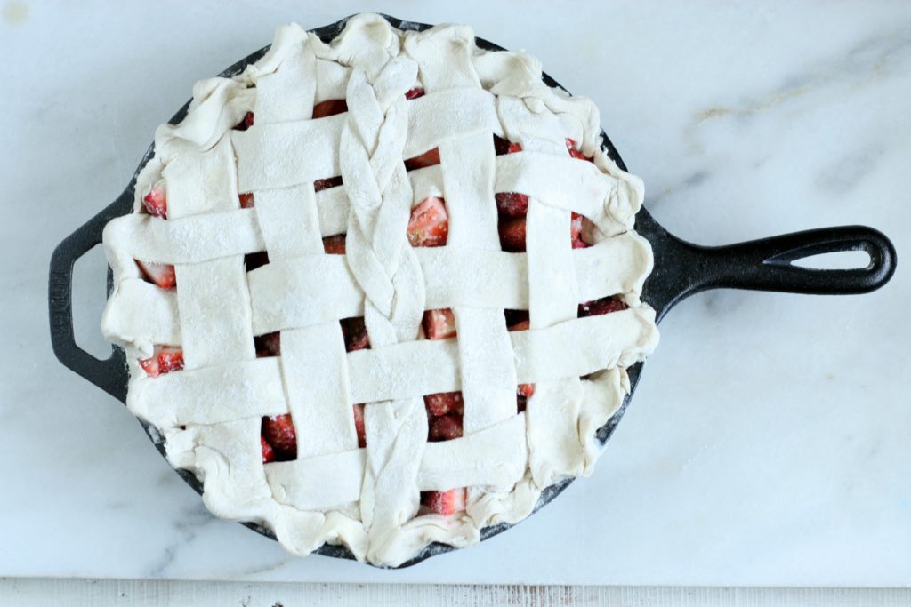 Unbaked strawberry Rhubarb Pie with a weaved crust in a cast iron skillet