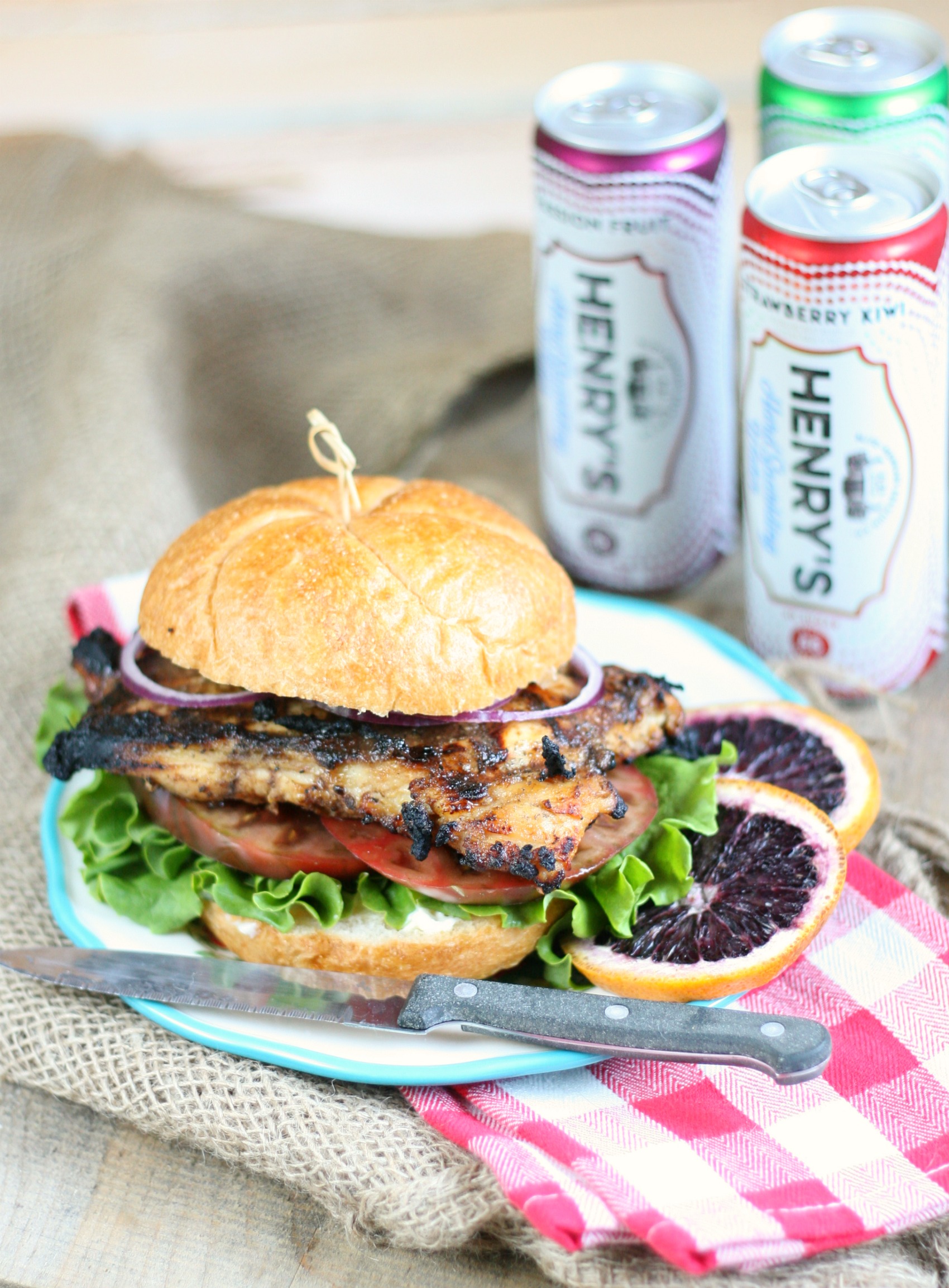 Grilled Chicken on roll with tomato slices, green leaf lettuce, and thinly sliced red onion on small plate.