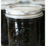 Homemade mixed berry jam in Mason jelly jars, sitting on light oatmeal color kitchen towel cooling.