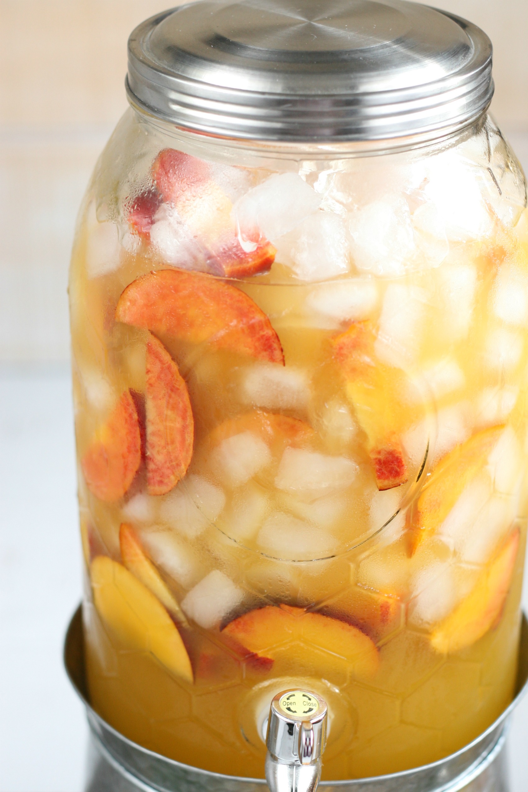 Close up of glass drink dispsenser filled with summer sangria, ice cubes, and peach slices.