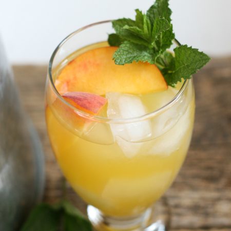 Summer sangria in clear footed glass with fresh peach slices, ice cubes, and a piece of fresh mint
