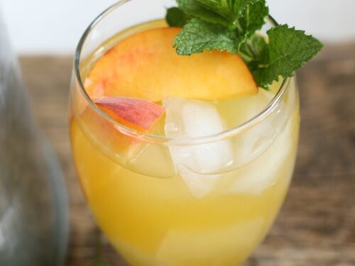Summer sangria in clear footed glass with fresh peach slices, ice cubes, and a piece of fresh mint