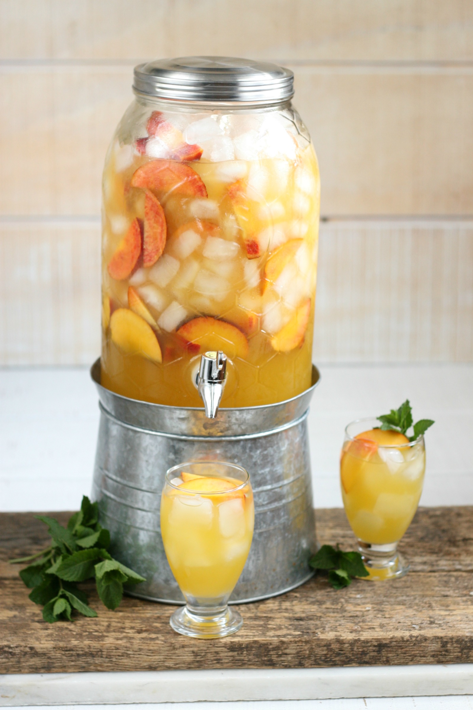 Summer sangria in a clear glass drink dispenser with aluminum screw on lid and sitting on galvanized footed base.