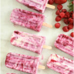 berry swirl popsicles laying on white marble surrounded by fresh berries