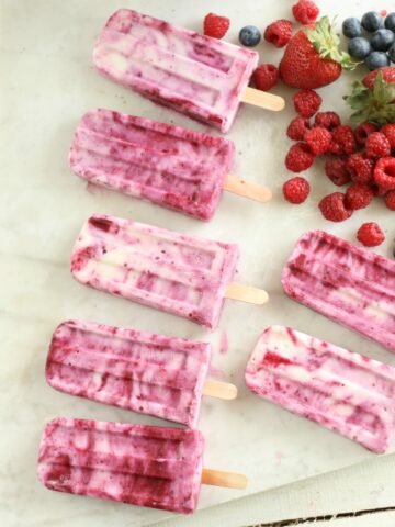 Berry Swirl Yogurt Pops laying on a piece of white marble with berries loose laying around the pops