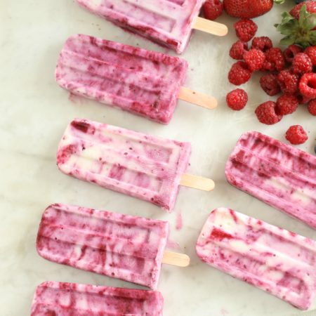 Berry Swirl Yogurt Pops laying on a piece of white marble with berries loose laying around the pops