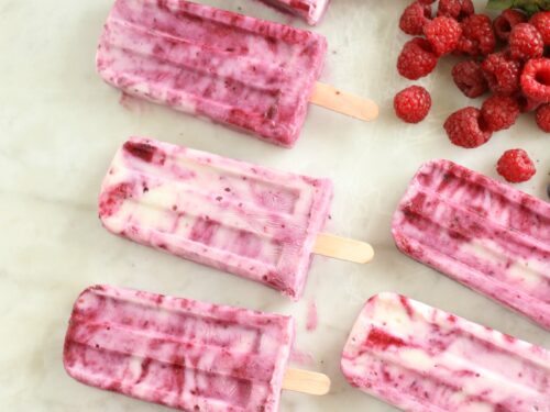Berry Swirl Yogurt Pops laying on a piece of white marble with berries loose laying around the pops