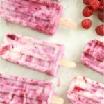 berry yogurt popsicles on white marble with fresh strawberries, blueberries, and raspberries around