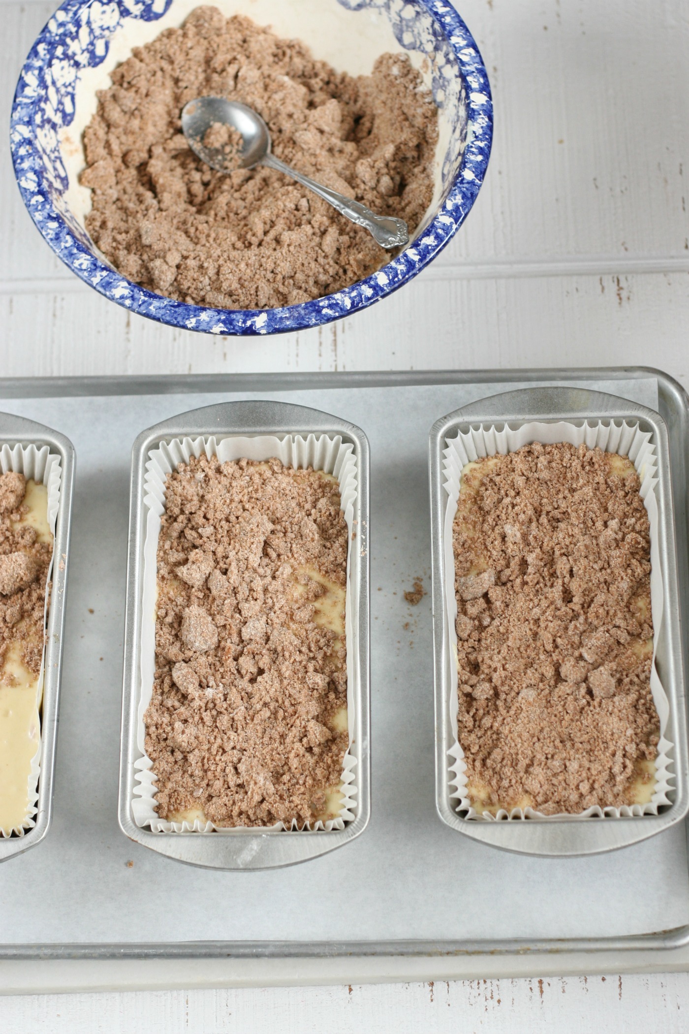 streusel topping being spooned onto coffee cake batter in loaf pans.