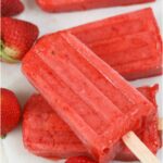 frozen strawberry popsicles on each other on white marble, fresh strawberries around