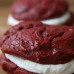 Red Velvet Whoopie Pies sitting on a butcher block filled with cream cheese frosting
