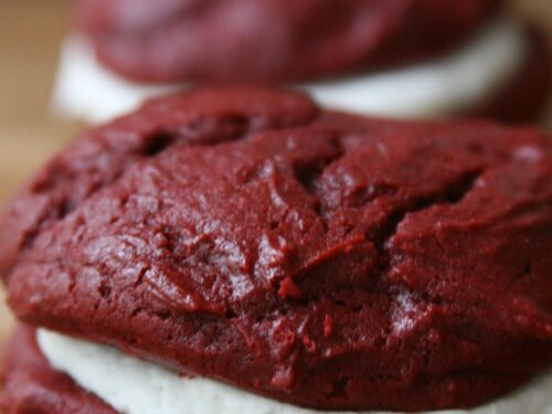 Red Velvet Whoopie Pies sitting on a butcher block filled with cream cheese frosting