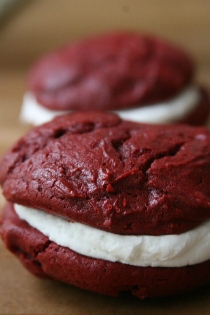 Red Velvet Whoopie Pies sitting on a butcher block filled with cream cheese frosting