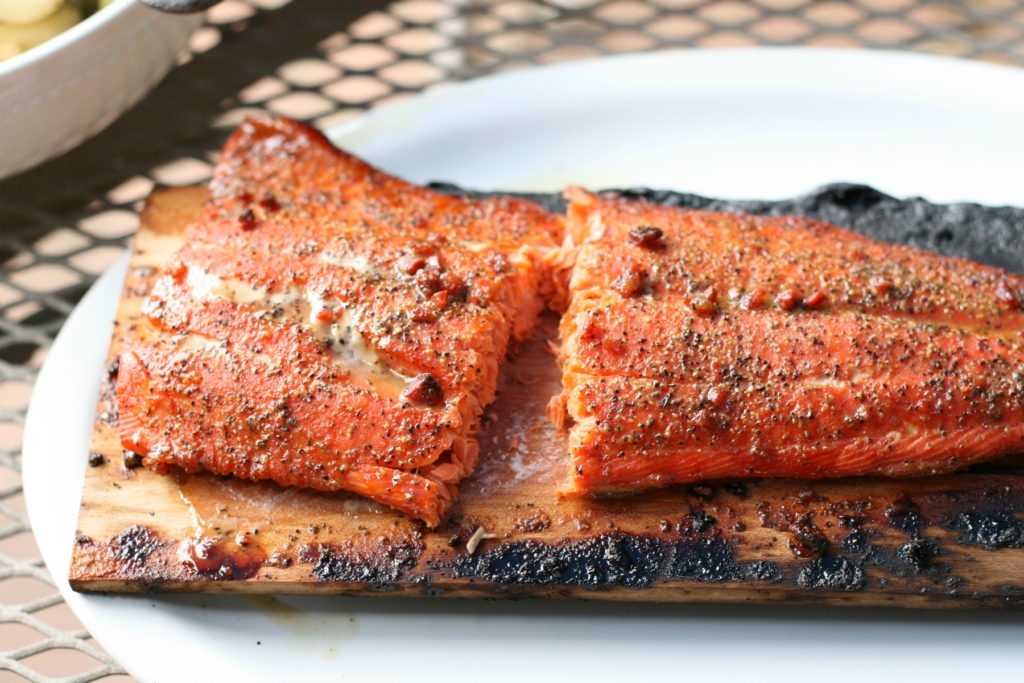 wild salmon on a wooden plank sitting on a white serving plate on a patio table