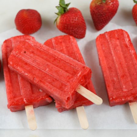 Strawberry frozen fruit bars sitting on each other with fresh strawberries around them