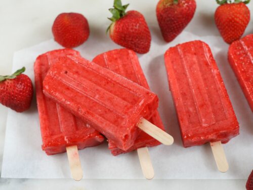Strawberry frozen fruit bars sitting on each other with fresh strawberries around them