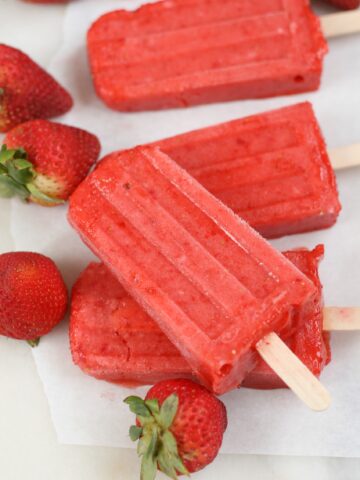 Strawberry Fruit bars stacked on top of each other on a piece of white marble with fresh strawberries scattered to the sides