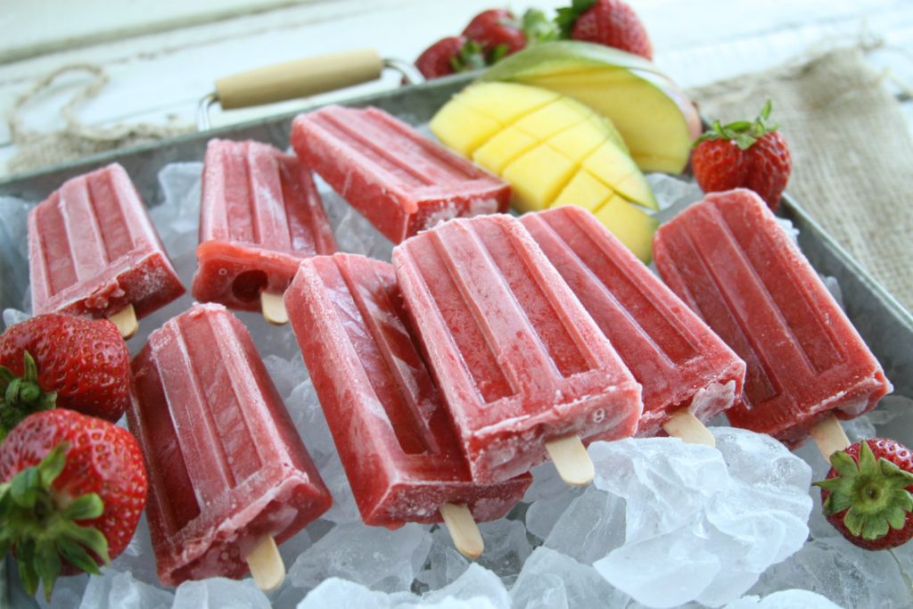 Strawberry Mango ice pops sitting in a layer of ice on a galvanized tray