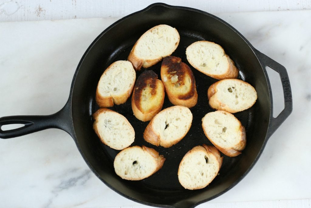 baguette slices in a cast iron being browned in olive oil