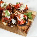 Bruschetta on a wooden cutting board with shaved Parmesan cheese and fresh basil