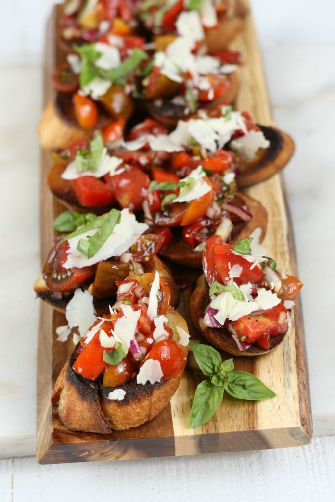 bruschetta on a cutting board with heirloom tomatoes and freshly shaved Parmesan cheese