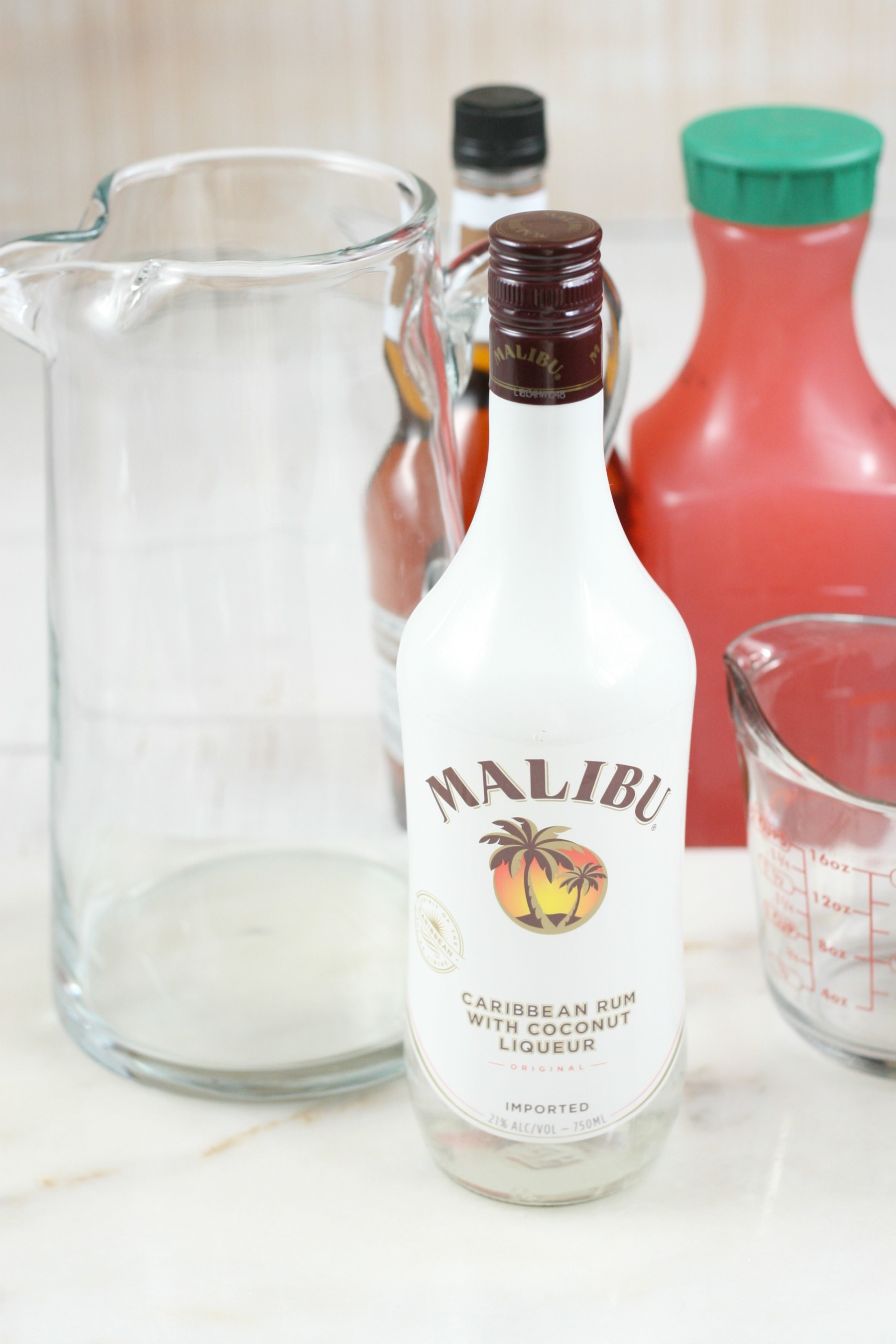 glass pouring pitcher with ingredients set to the side, raspberry lemonade, amaretto, and malibu.