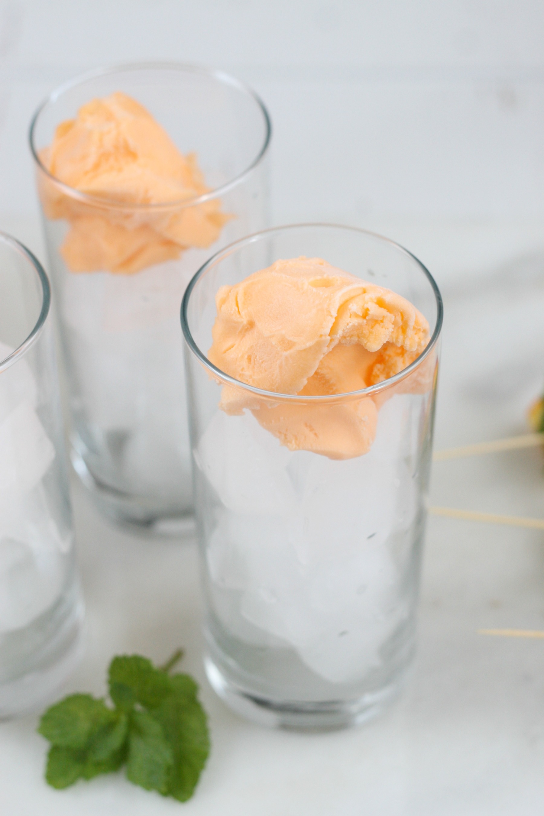 scoops of orange sherbert in cocktail glasses filled with ice.