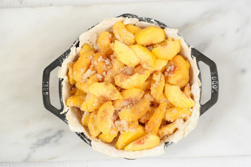 2 handle cast iron pan with peaches in a bottom crust