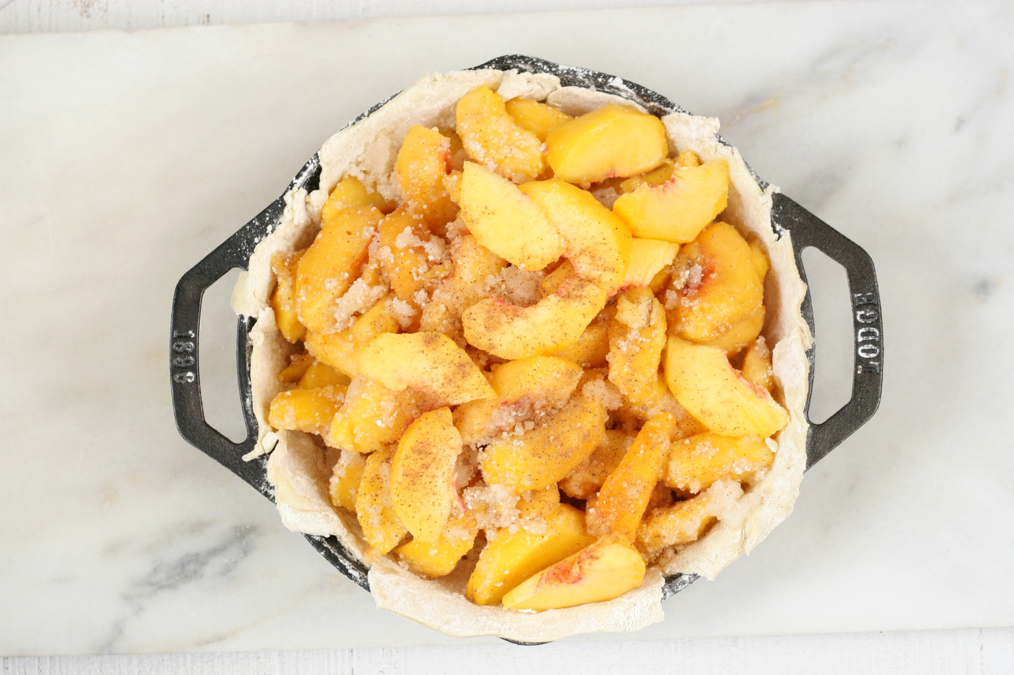 2 handle cast iron pan with peaches in a bottom crust.