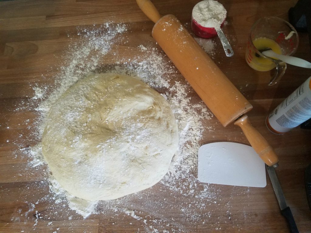 homemade cinnamon rolls being rolled out on a butcher block