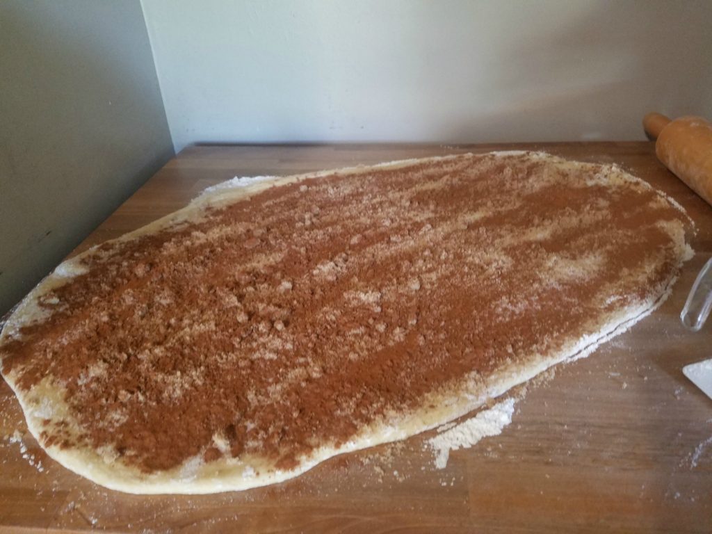 brown sugar, sugar, and cinnamon sprinkled on top before being rolled up. Wooden rolling pin to the right