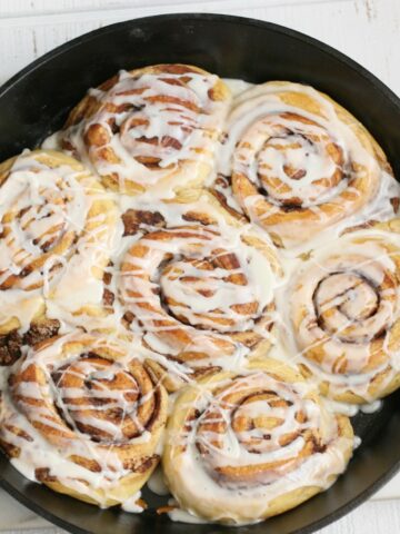 cinnamon rolls in a cast iron pan drizzled with icing