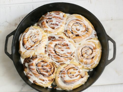 cinnamon rolls in a cast iron pan drizzled with icing