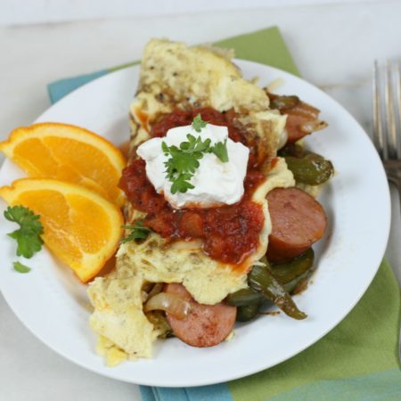 sausage fajita omelet on a white plate with orange slices to the left