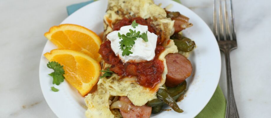 sausage fajita omelet on a white plate with orange slices to the left