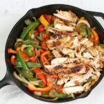 grilled chicken and sauteed onions and multi colored bell peppers in a cast iron skillet