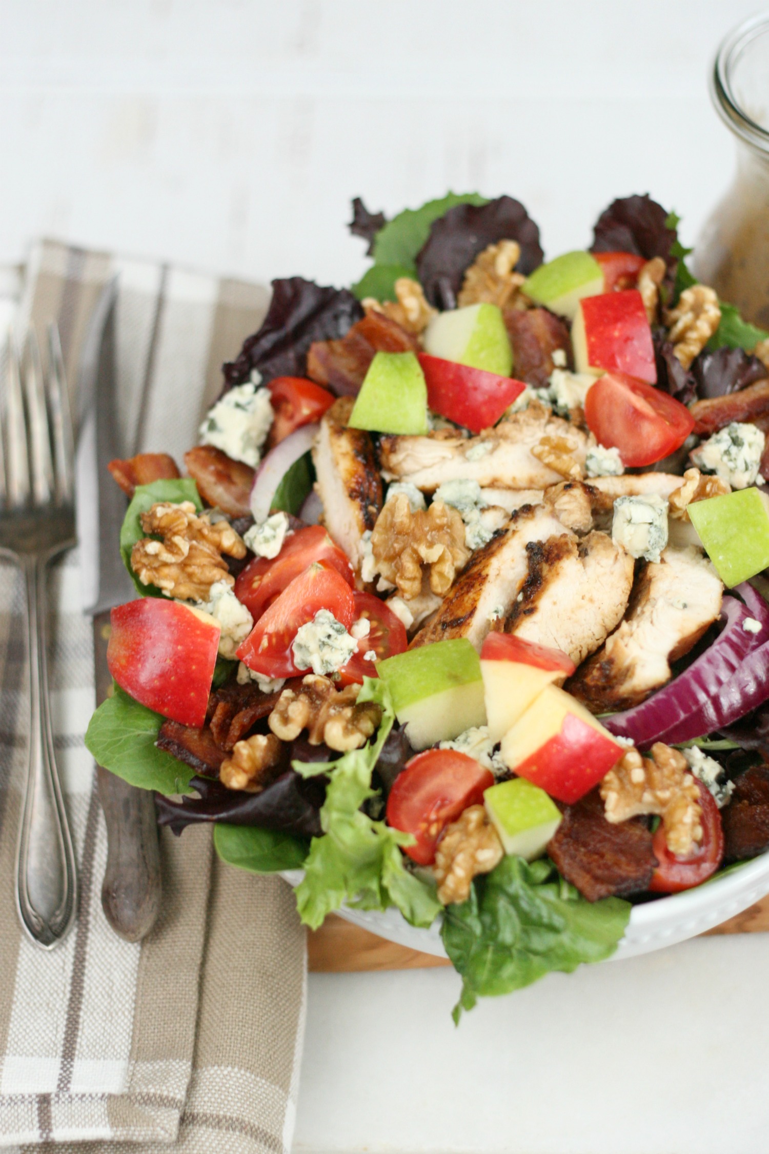 Harvest chicken salad with mixed baby greens, slices of red onions, walnuts, chunks of blue cheese, red and green apple chunks.