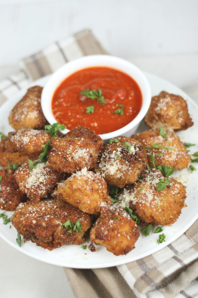 parmesan crusted chicken bites with marinara sauce and sprinkled with freshly grated Parmesan cheese on a small plate