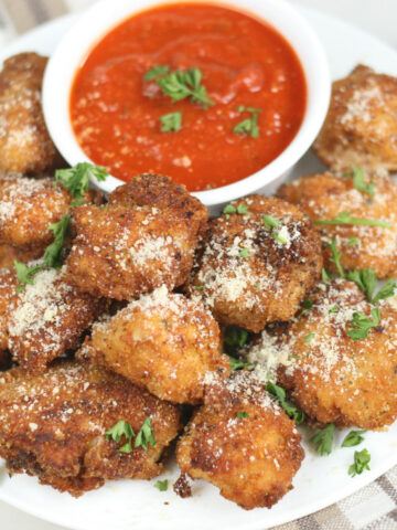 parmesan crusted chicken bites piled up high on a small plate and served with a small cup of warm marinara sauce