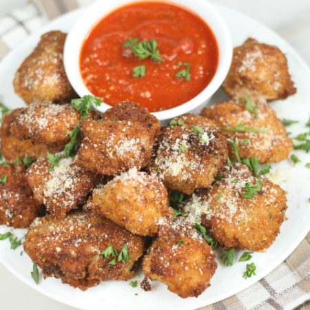 parmesan crusted chicken bites piled up high on a small plate and served with a small cup of warm marinara sauce