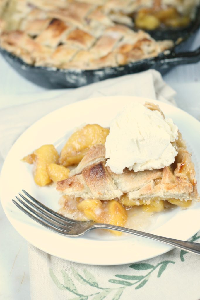 slice of homemade peach pie with vanilla ice cream on top on a white glass plate with fork