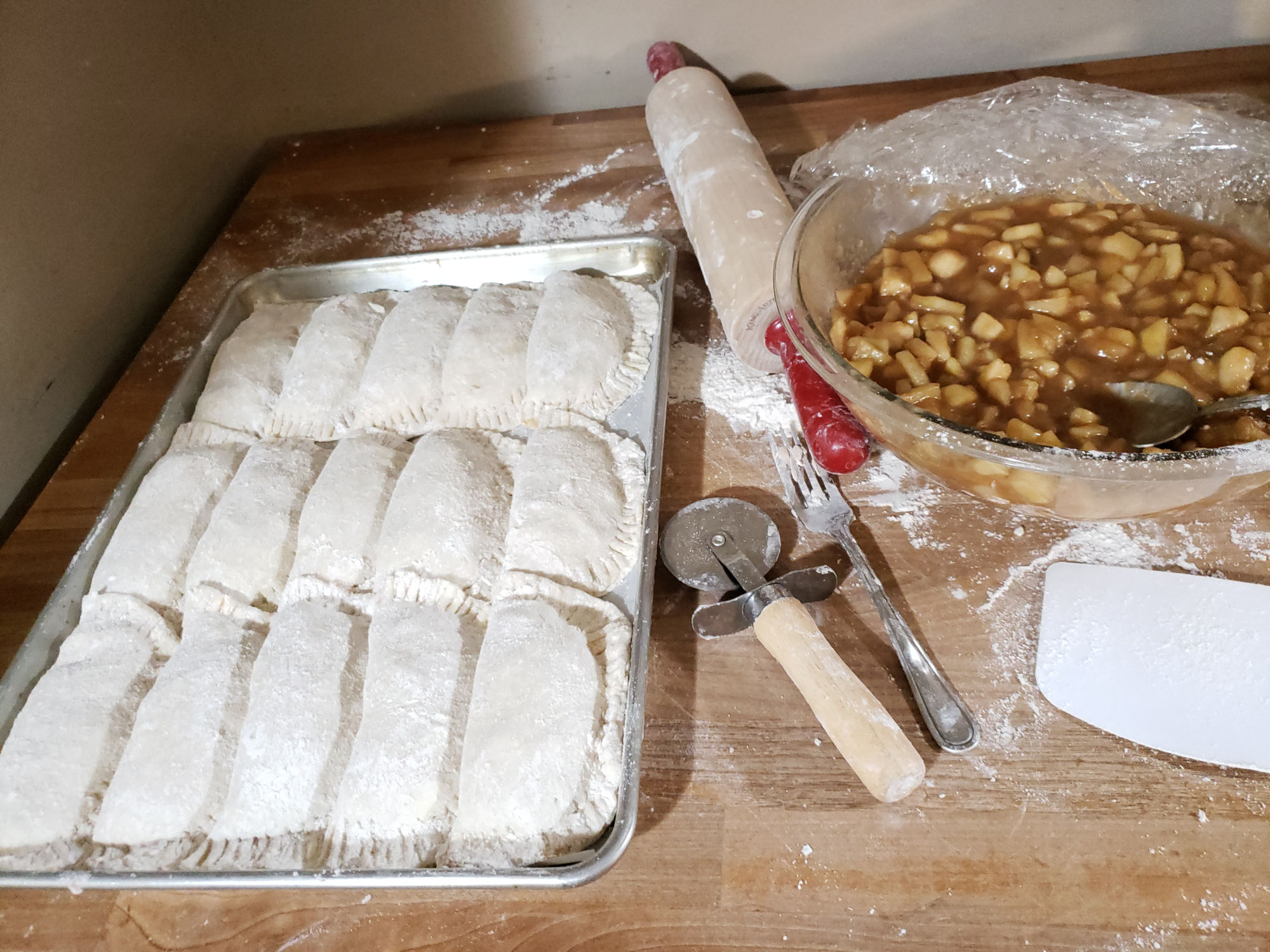 apple hand pies on a half sheet pan and apple filling in a bowl to the side.