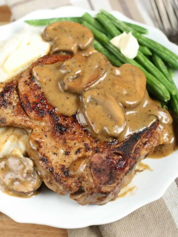cast iron pork chops with a mushroom cream sauce and mashed potatoes on a white plate