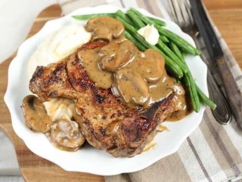 cast iron pork chops with a mushroom cream sauce and mashed potatoes on a white plate