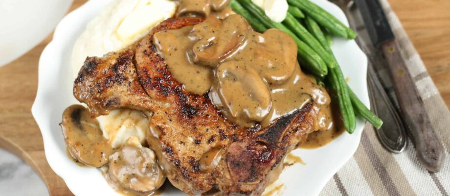 cast iron pork chops with a mushroom cream sauce and mashed potatoes on a white plate
