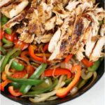 chicken fajitas in cast iron skillet with multi colored bell peppers