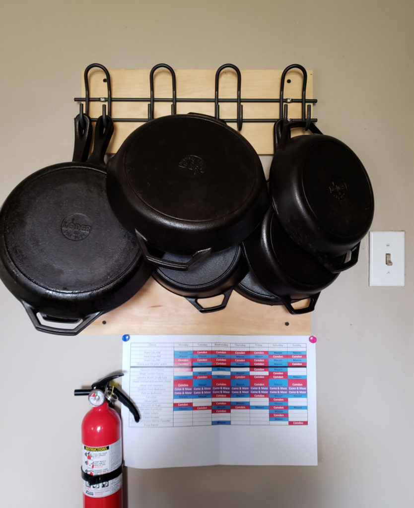 cast iron pans hung on the wall in a kitchen on hooks on a piece of wood.