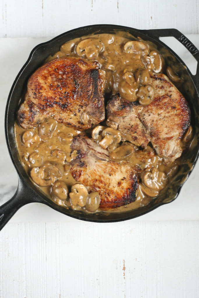 browned pork chops and mushroom sauce in a cast iron skillet